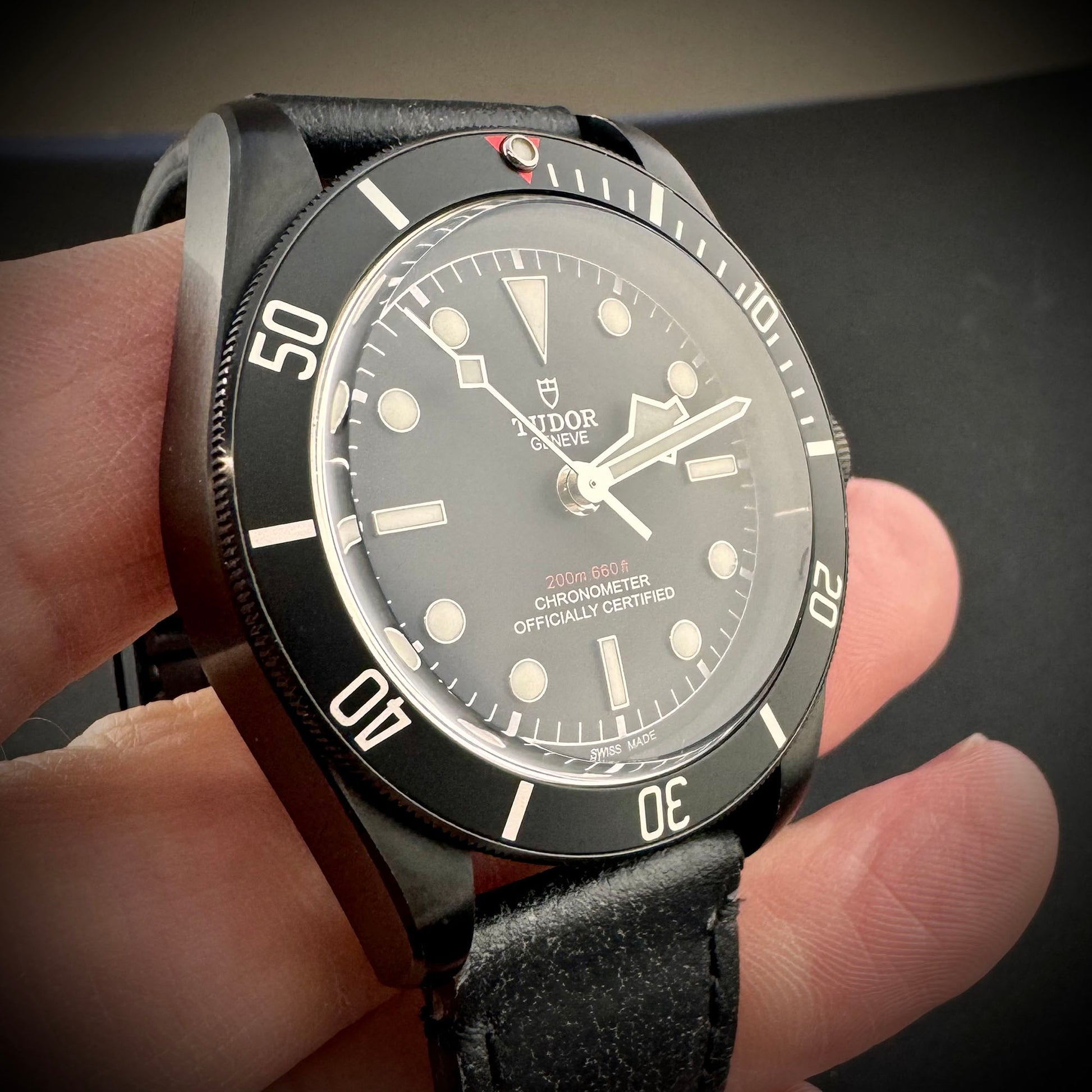 Black wristwatch with visible brand name held in a hand against a dark background