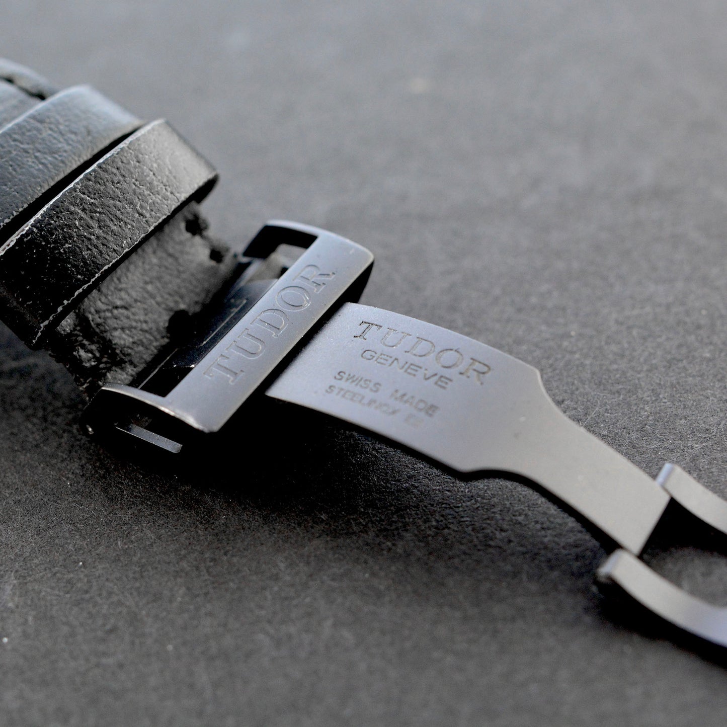 Close-up of a Tudor watch strap on a gray surface