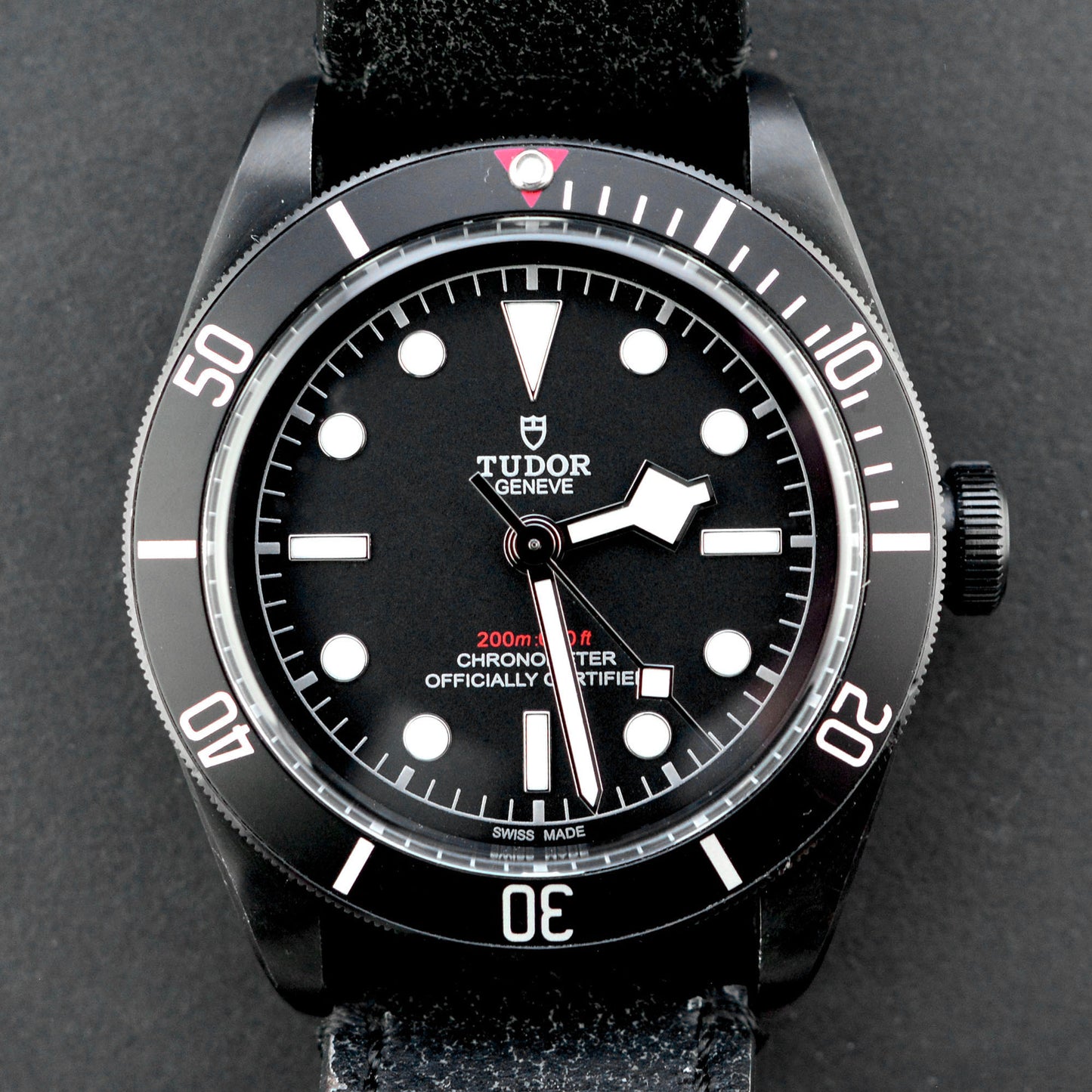 Tudor watch with black dial and leather strap on a dark background